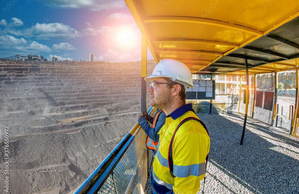 Worker in hard hat and safety vest looks out over a stone quarry from inside an observation deck