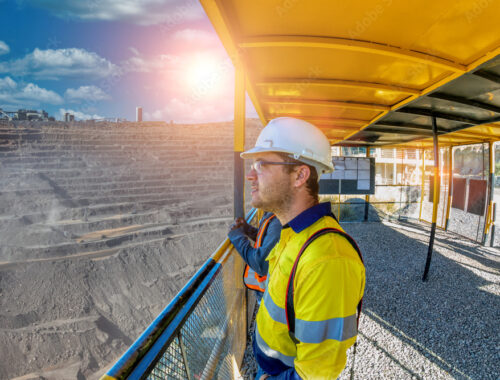 Worker in hard hat and safety vest looks out over a stone quarry from inside an observation deck