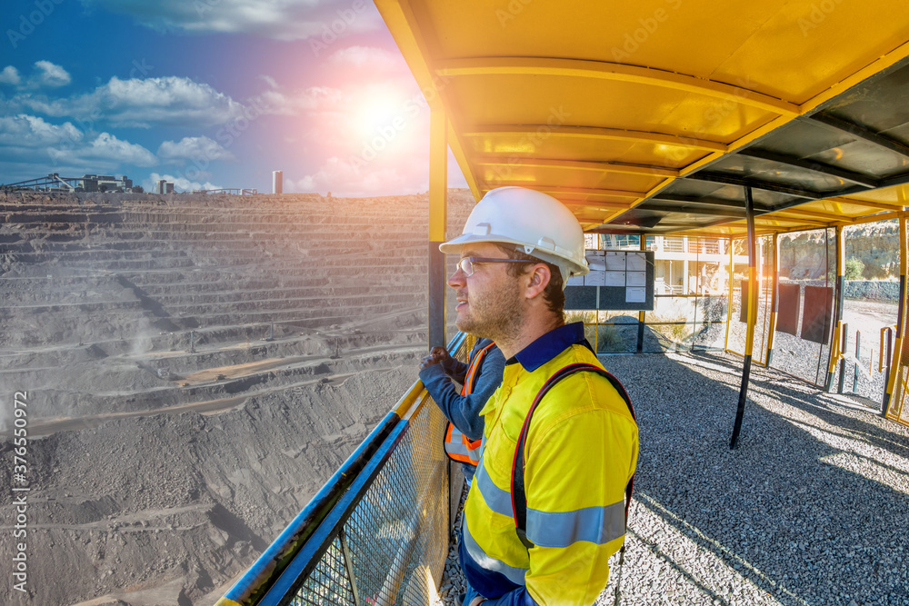 Worker in hard hat and safety vest looks out over a stone quarry from inside an observation deck