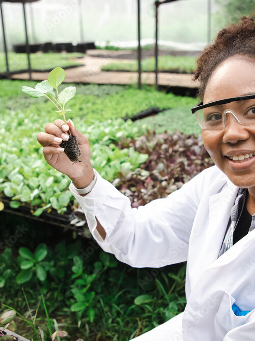 Woman in lab coat in a green house holding