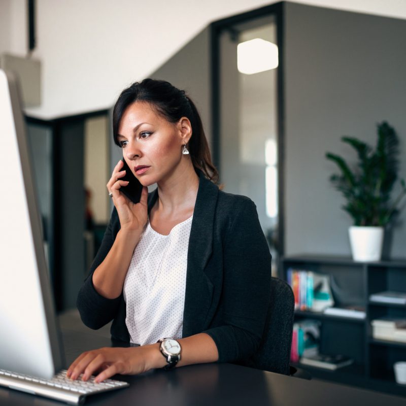 Person at a laptop while using a cell phone.